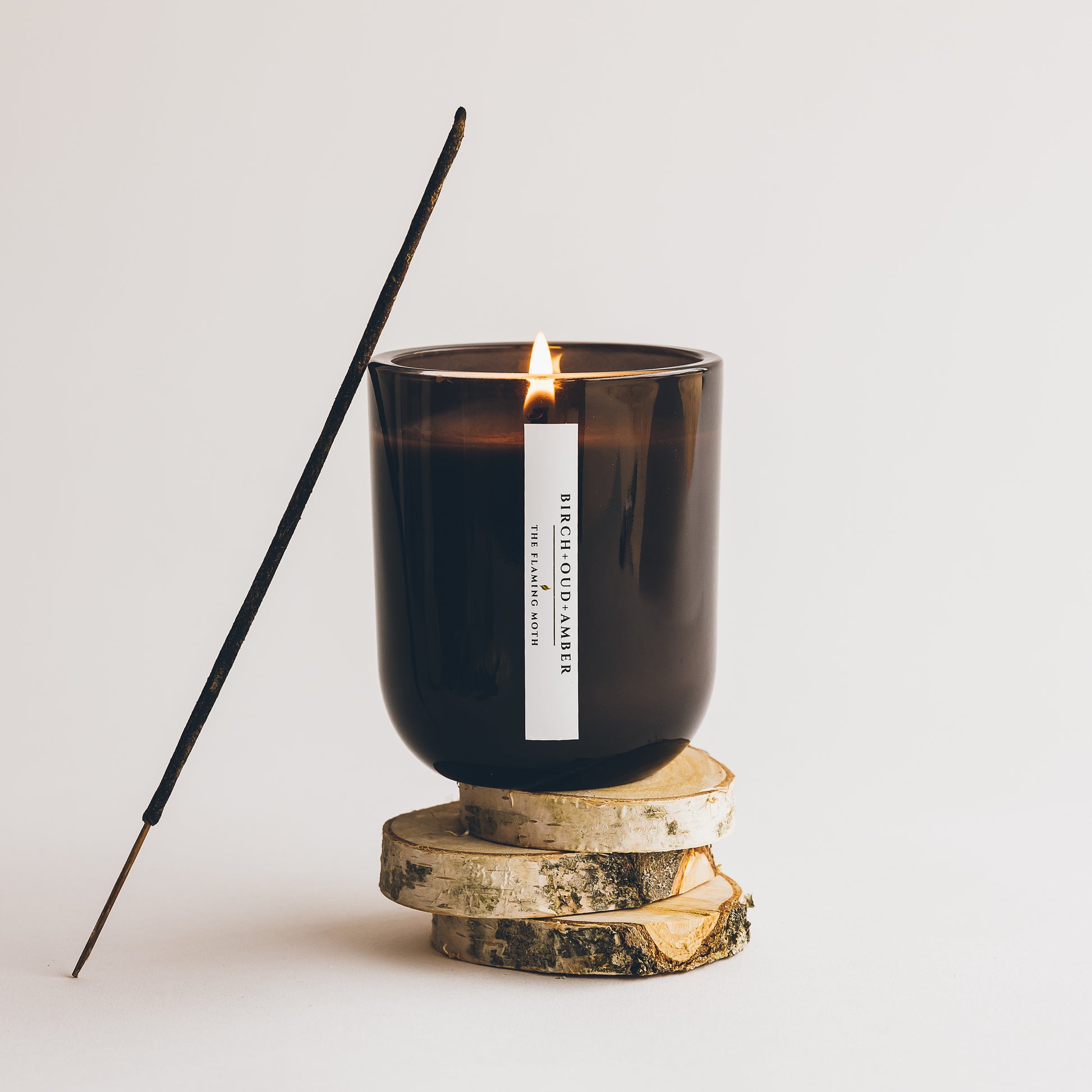 birch oud amber candle sitting on top of birch wood slices with an incense stick