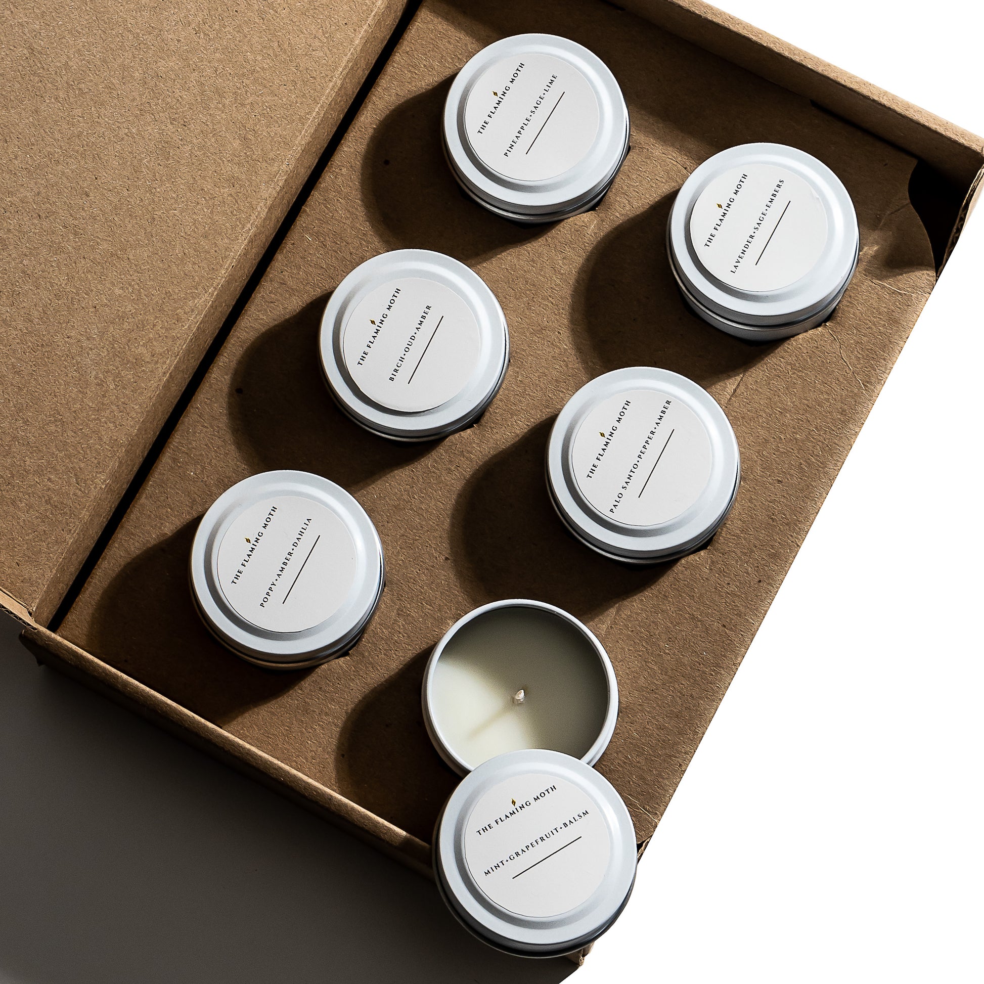 Set of six small candles in white tins in a cardboard box