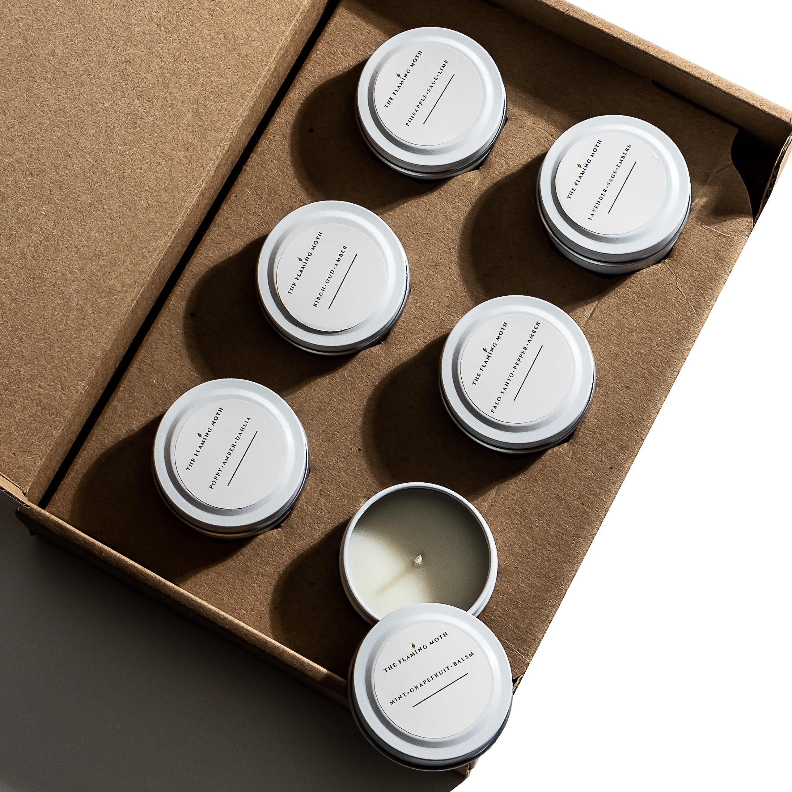 Set of six small candles in white tins in a cardboard box