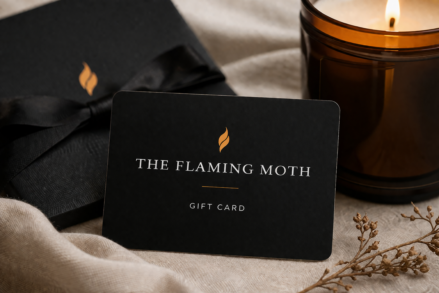 Black gift card for 'The Flaming Moth' with a lit candle and bow in the background.