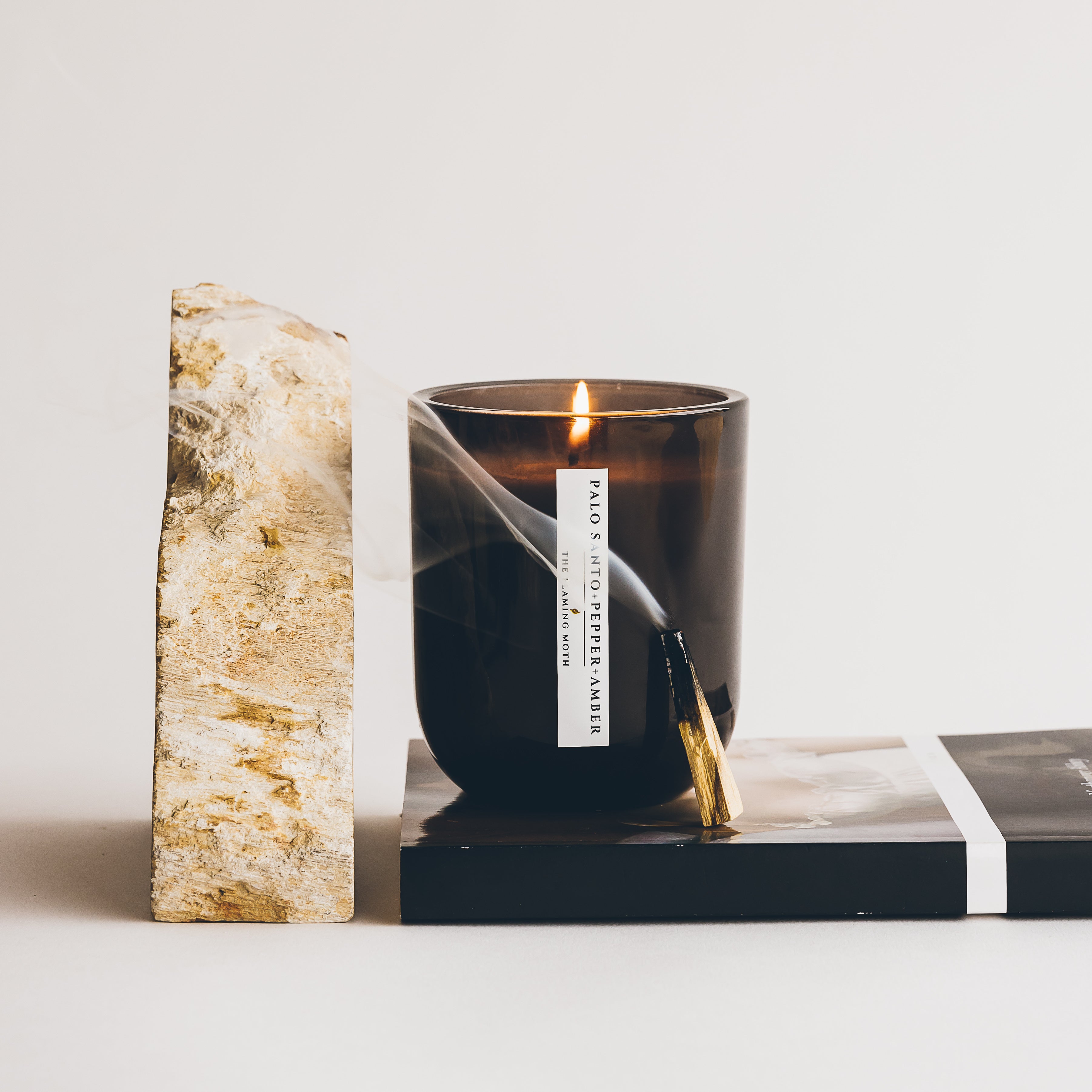 palo santo pepper amber candle with burning palo santo next to rock