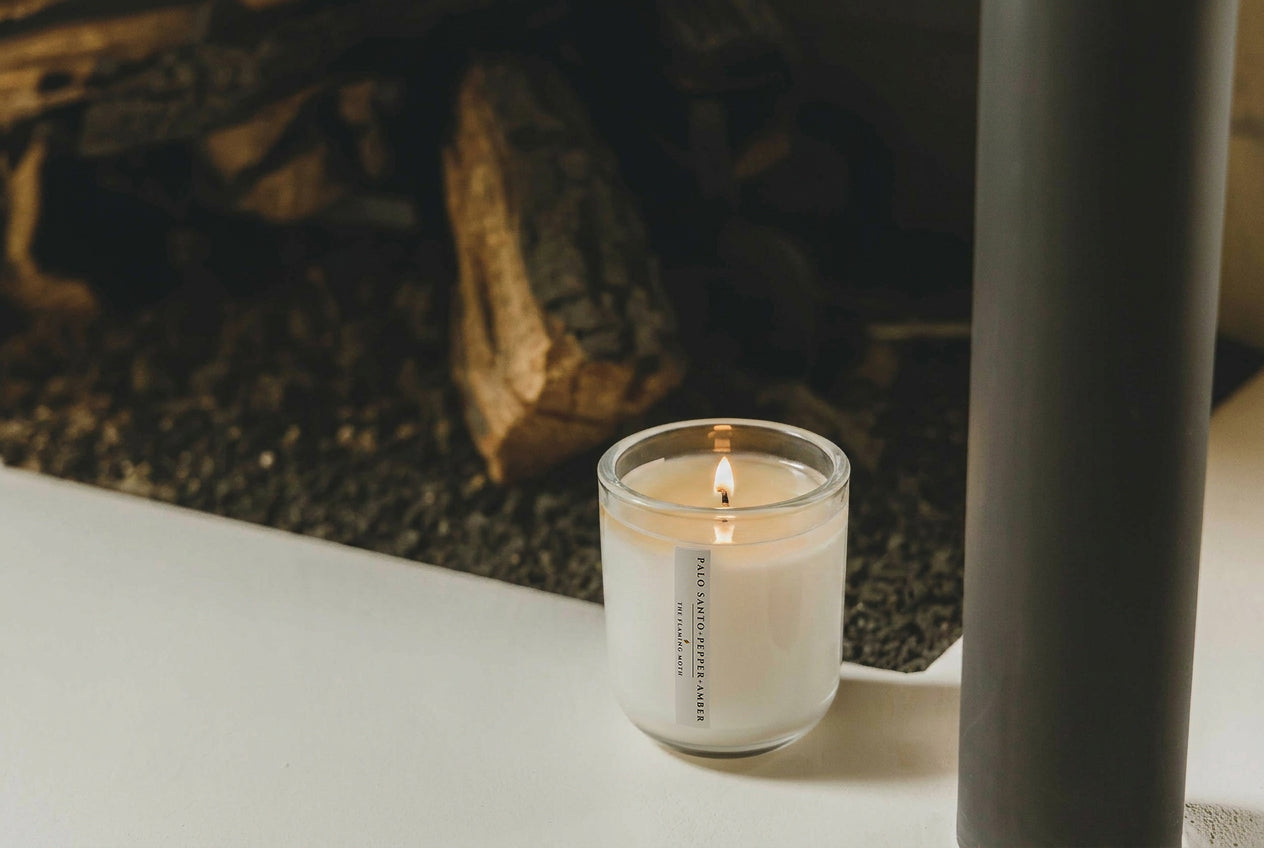 Candle in a glass holder on a surface with a fireplace in the background