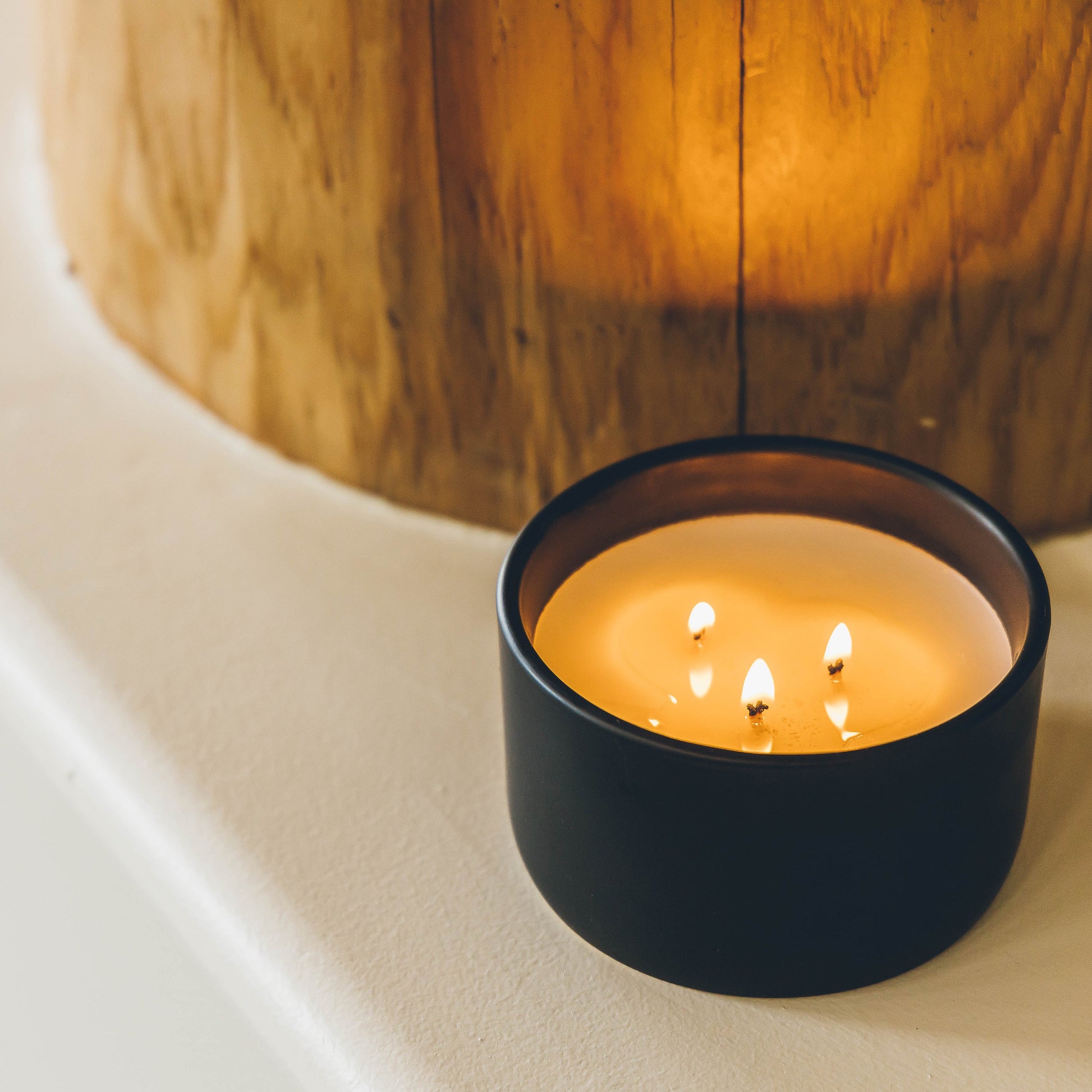 three wick candle in a black ceramic vessel next to wood sculpture